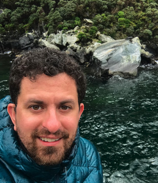 man with brown hair in a blue jacket by water