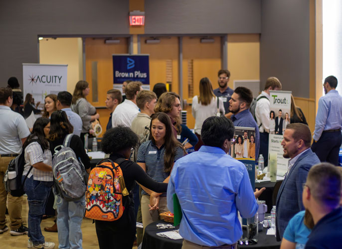 Crowded networking event with company booths and informational displays.